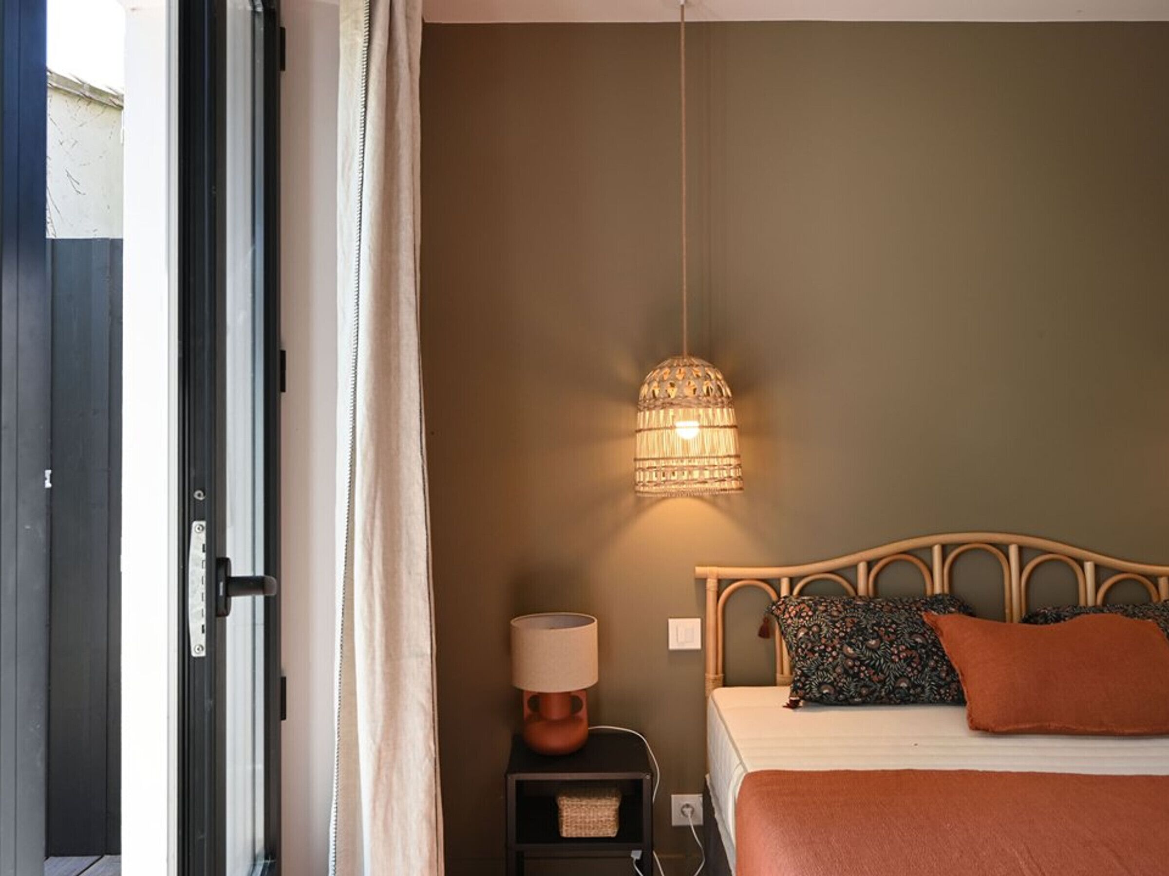 Un dormitorio con cama, lámpara de noche, lámpara colgante y una puerta.