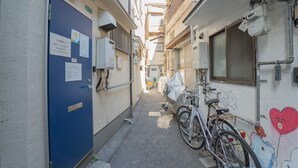 A narrow alleyway with a blue door, bicycles, and a wall with a cartoon character.