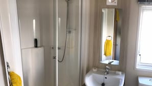 A bathroom with a glass shower enclosure, a white sink, a mirror, and a window.