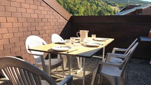 A patio with a table set for two, surrounded by white plastic chairs, overlooking a forested hillside. - Charming Duplex at the Foot of Corrençon Slopes (Corrençon-en-Vercors)