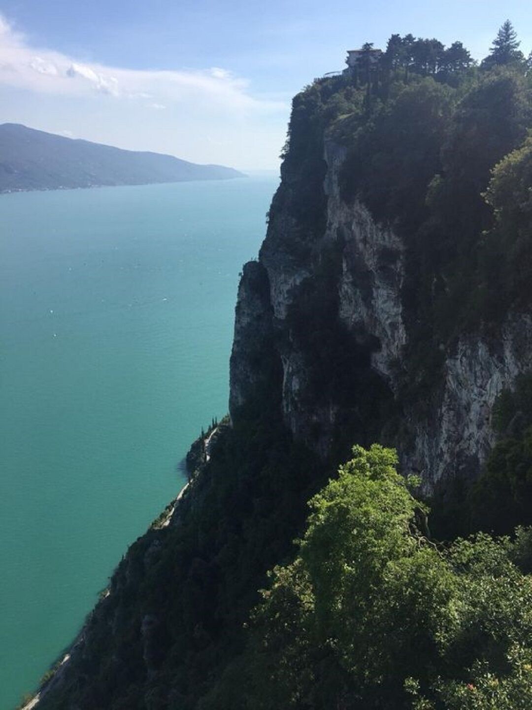 A coastal cliff with a view of the sea and distant mountains.