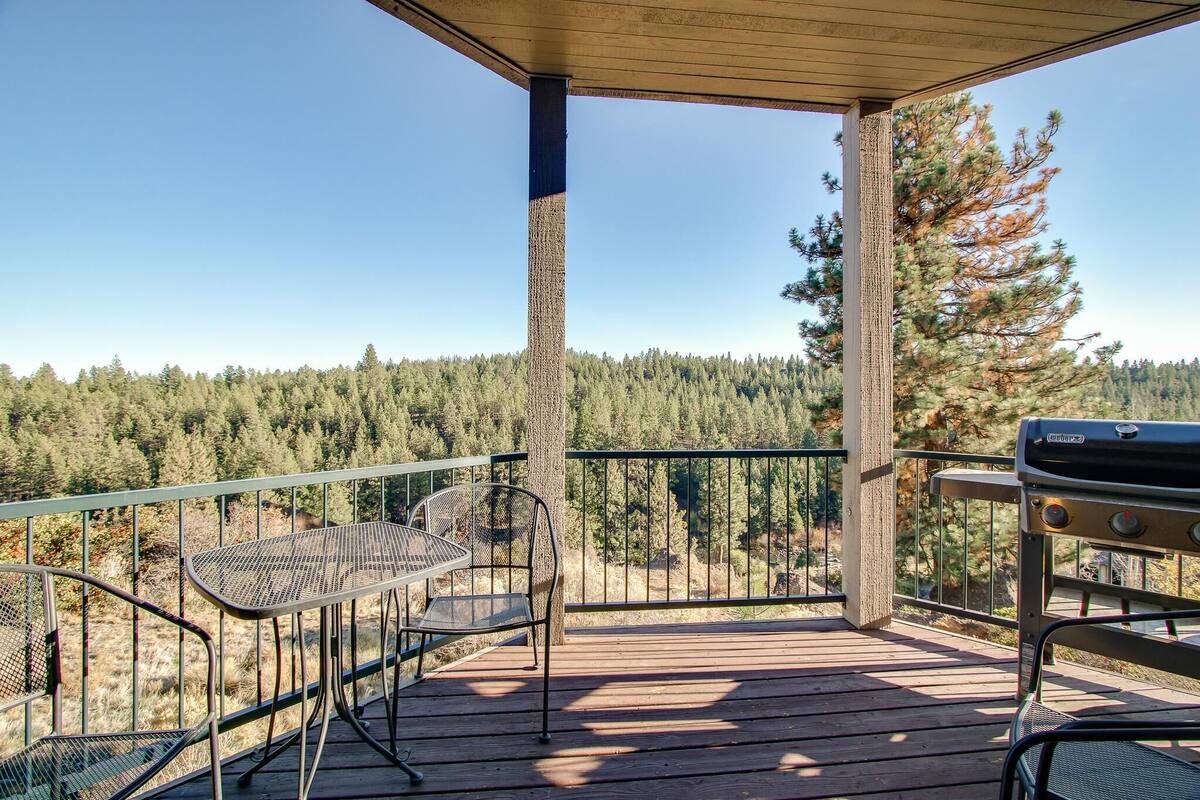 A wooden deck with metal chairs and a grill, overlooking a forested area.