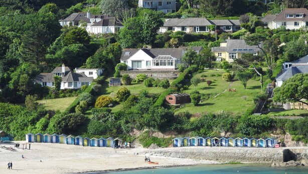 A coastal area with a sandy beach, a row of beach huts, and houses on a hillside.