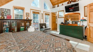 A spacious bedroom with a large bed, wooden ceiling, and a television mounted on the wall. - BlackDog Hideaway_Hot Tub, (2) Arcades, Foosball, PingPong, Smart Tv's, Cable + HOA Amenity Passes (Truckee)
