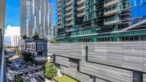 Un immeuble moderne de grande hauteur, doté de nombreux balcons et de grandes fenêtres, entouré d’autres bâtiments imposants et surplombant une rue animée.