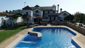 A swimming pool with a tiled edge, a grassy area, and a building with a white facade and red-tiled roof. - Holiday Home ‘La Cazuela’ with Mountain View, Pool, Garden & Terraces (Arcos de la Frontera)
