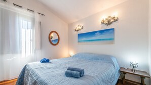 Een slaapkamer met een groot bed, een nachtkastje, een wandlamp, een schilderij en een spiegel.