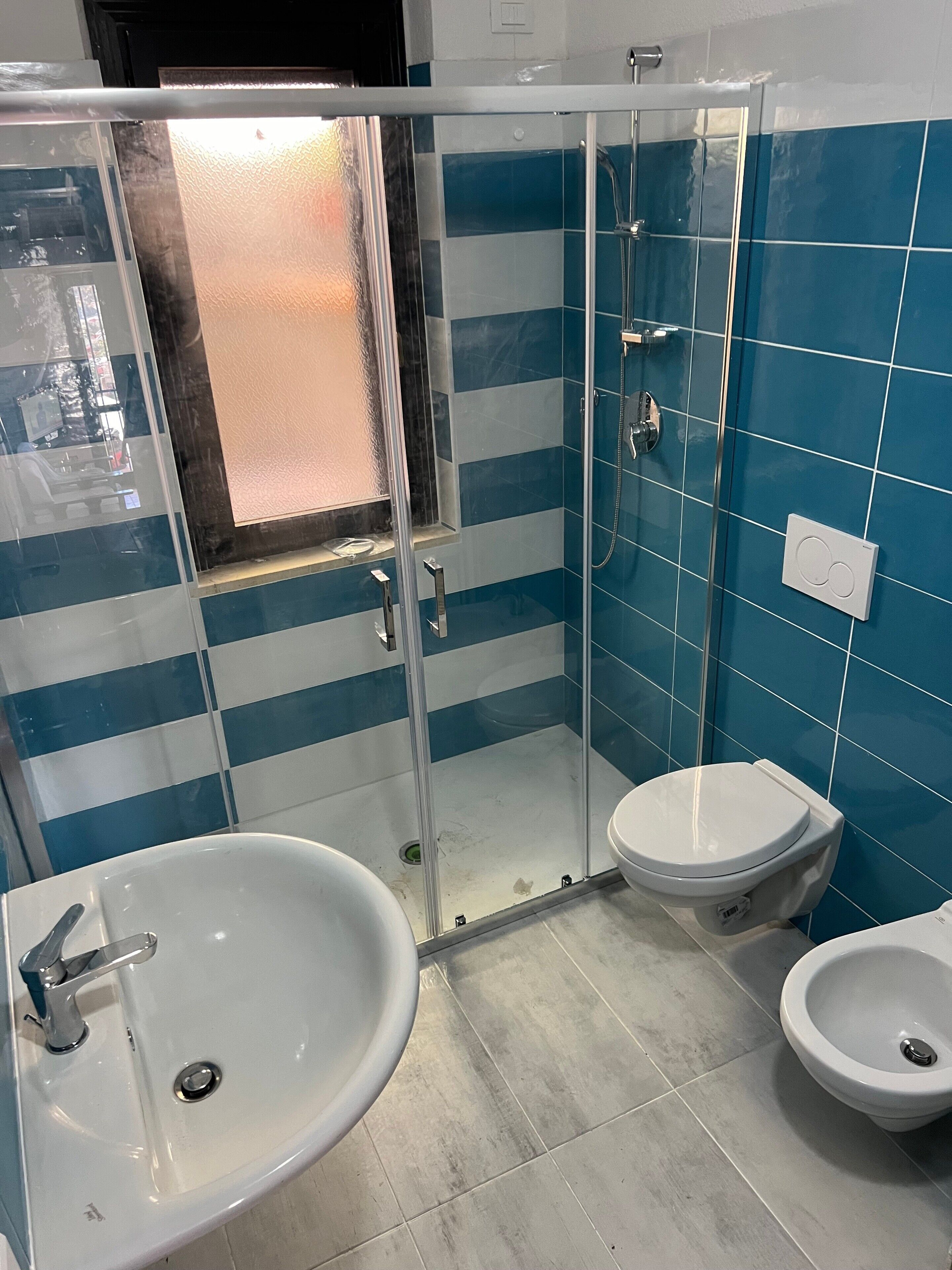 A bathroom with a glass-enclosed shower, a sink, and two toilets.