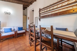 Une pièce comprenant une table à manger en bois, deux chaises en bois, un canapé avec des coussins bleus et un mur blanc orné d’un élément décoratif en métal.