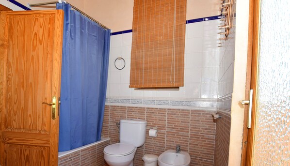 Une salle de bain avec une porte en bois, un rideau de douche bleu, des toilettes, un lavabo et un porte-serviettes.