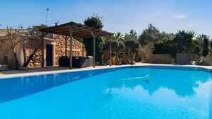 Ein Schwimmbecken mit einem Steinhaus und einer Pergola im Hintergrund.