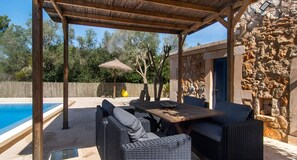 Un espacio exterior cubierto con piscina, mobiliario de mimbre y pared de piedra.