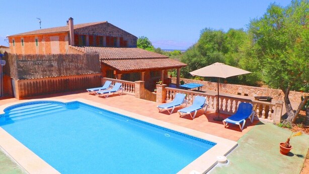 A swimming pool with lounge chairs, a covered patio, and a stone building with a tiled roof. - Tranquil country house Can Guillem with pool, terrace, Wi-Fi and air conditioning (Campos)
