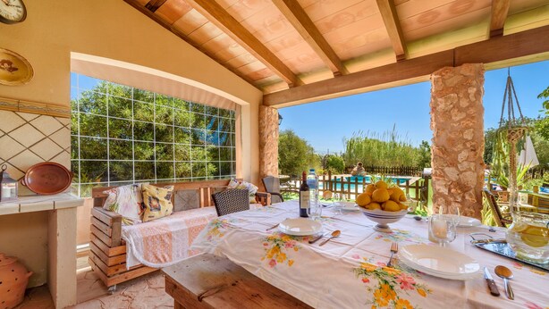 A covered patio with a table set for dining, a stone pillar, and a view of greenery. - Finca "Son Antem" with private pool, garden, terrace, and Wi-Fi (Llucmajor)