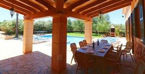 Une terrasse extérieure avec une piscine, un sol en pierre et une table dressée pour les repas.