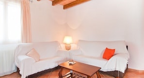 Une pièce avec deux canapés blancs, une table basse en bois, une lampe et une fenêtre ornée de rideaux légers.