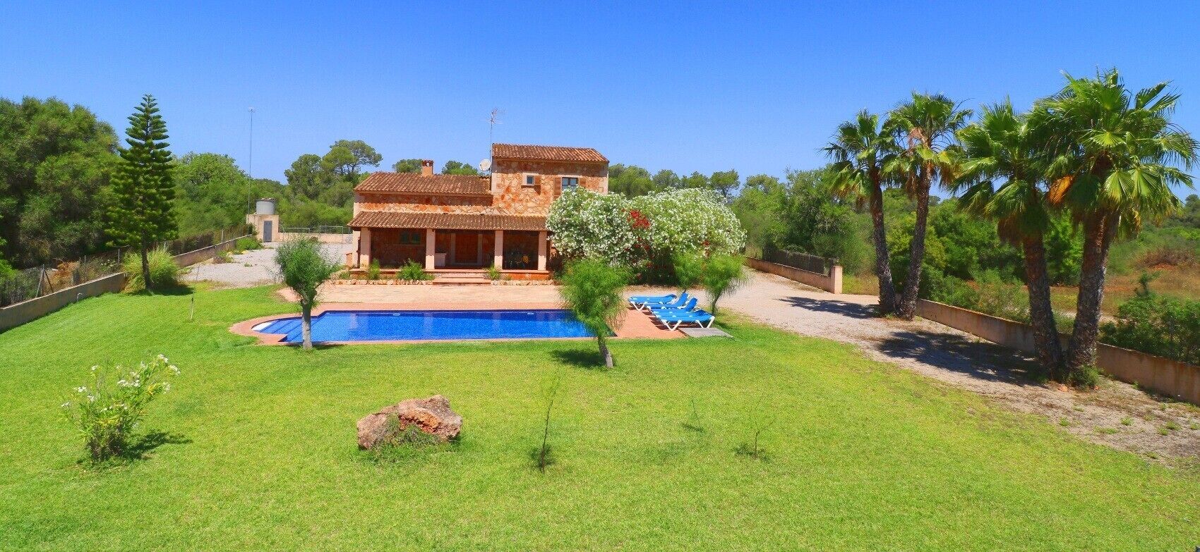 Una casa de dos pisos con piscina, rodeada de césped cuidado y palmeras.