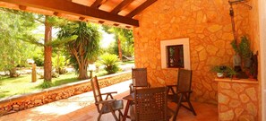 Une terrasse couverte avec des murs en pierre, des chaises en bois et une petite fenêtre.