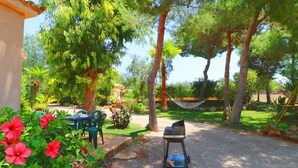 Un jardin avec un hamac, un barbecue et une table avec des chaises.