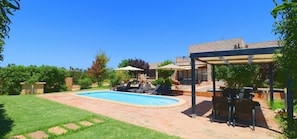 Un patio trasero con piscina, mobiliario exterior y una pérgola.