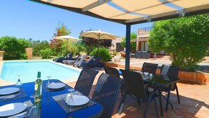 Zona junto a la piscina con sillones de descanso, sombrillas y una mesa para dos.