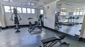 Un gimnasio con equipo de ejercicio, espejos y grandes ventanales.