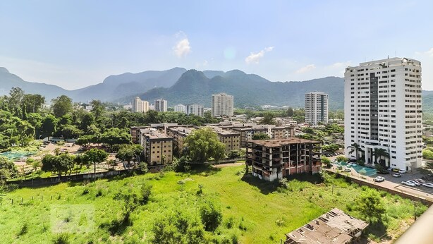 Zona residencial con varios edificios de apartamentos, un amplio campo cubierto de césped y montañas al fondo.