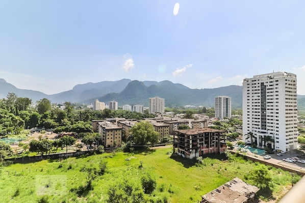A residential area with multiple apartment buildings, a large open grassy field, and mountains in the background. - Rio Plaza - Suítes no Rio de Janeiro por Carpediem (Rio de Janeiro)