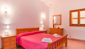 Une chambre à coucher avec un lit en bois, des tables de chevet avec des lampes, une commode, un miroir et une fenêtre avec des stores.