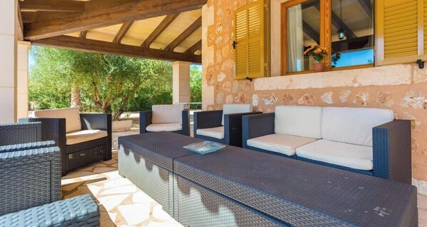 Un patio exterior con mobiliario de mimbre, una pared de piedra y una ventana con contraventanas.