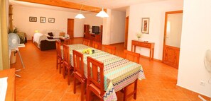 Un comedor con una mesa lista para cuatro, sillas de madera, un televisor y un mueble pequeño.