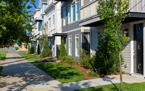 Row of townhouses with uniform architecture, featuring a combination of siding and windows, set amidst well-manicured lawns.
