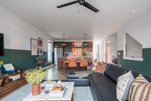 Relax in this open-plan living space with a sofa set against a vibrant accent wall, a central island kitchen, and modern pendant lighting.