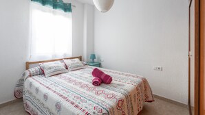 Un dormitorio con cama, una ventana con cortinas, una mesita de noche y una lámpara colgante.