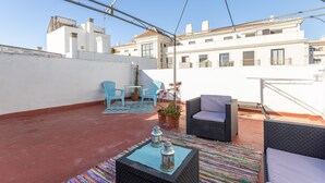 Una terraza en la azotea con mobiliario exterior, plantas en macetas y vistas despejadas de los edificios circundantes.