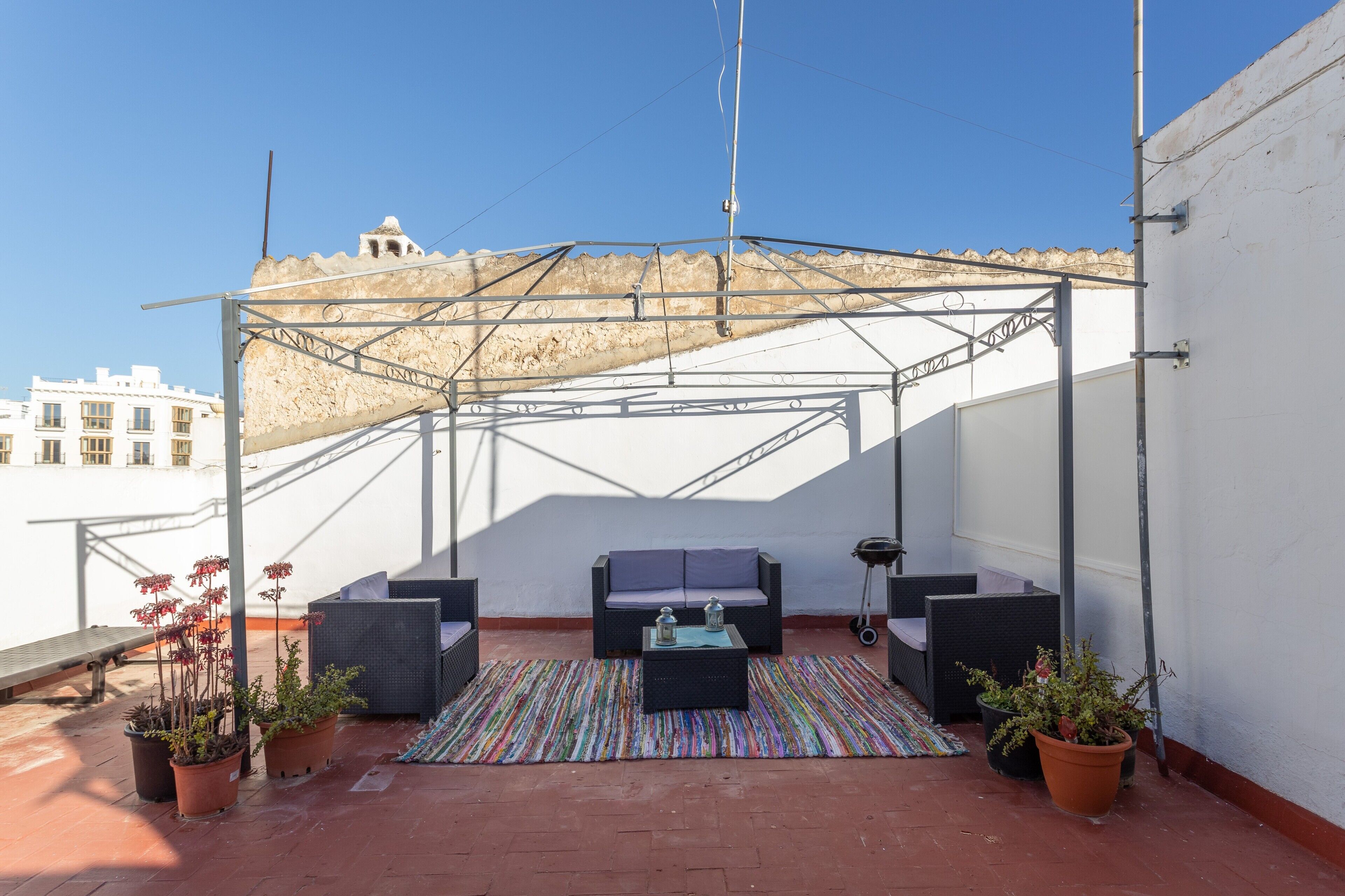 A rooftop terrace with a covered seating area, potted plants, and a view of the cityscape.