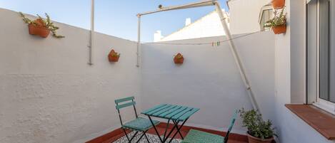 A small outdoor patio with a table and chairs, potted plants, and a white wall.