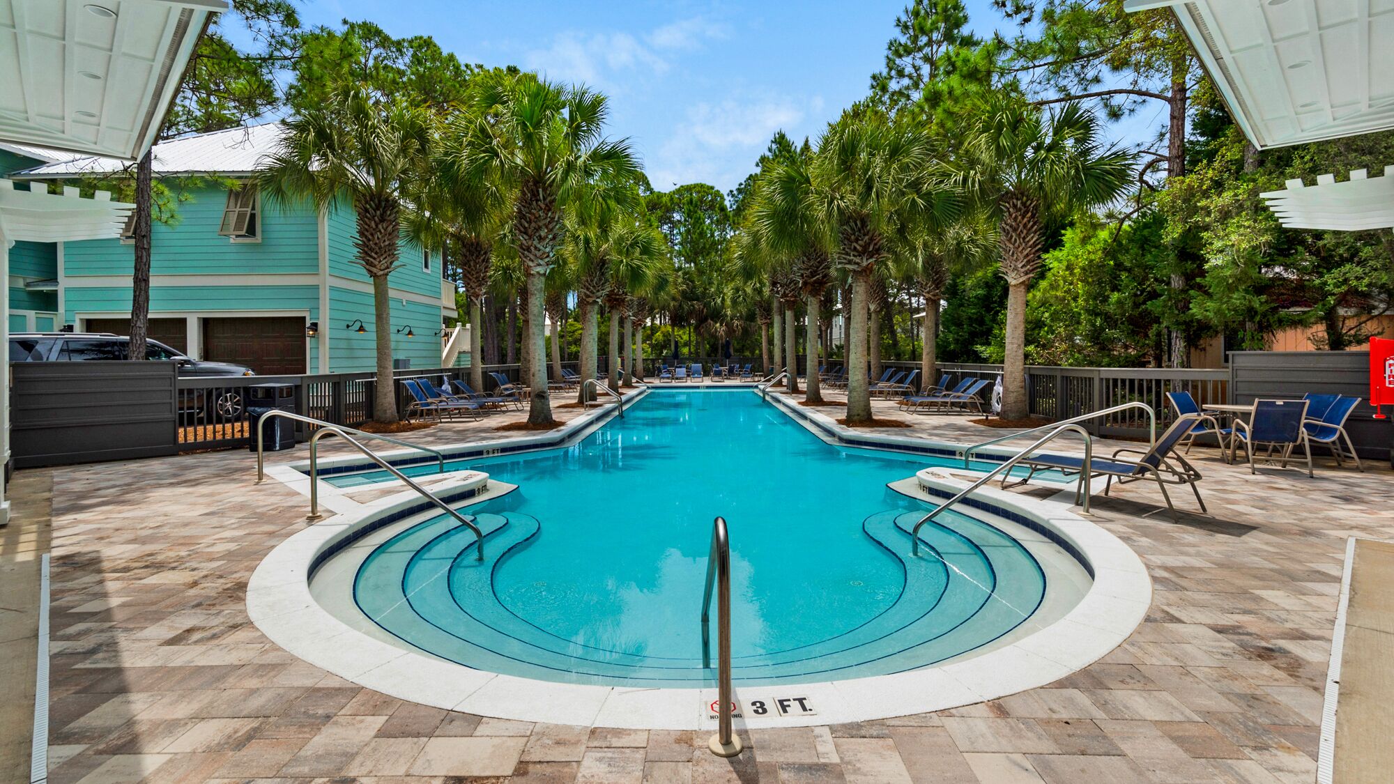 A swimming pool with a 3 FT depth marker, surrounded by lounge chairs and palm trees, with a building in the background.