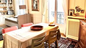Une pièce chaleureuse comprenant une table à manger, des chaises, une bibliothèque, un canapé et une fenêtre avec des rideaux.