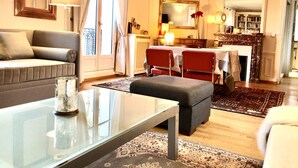 Un salon comprenant un canapé, une table basse en verre, une cheminée et un coin repas avec des chaises et une table.