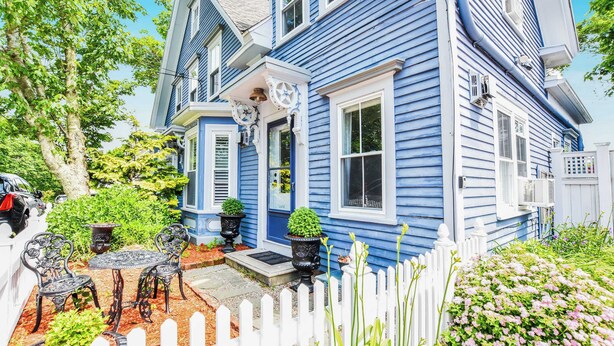 A blue house with a white picket fence, a patio with chairs and a table, and a small garden with pink flowers. - Gas Fireplace Front Patio & Parking Spot! (Provincetown)