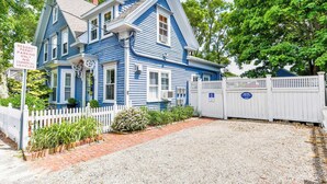 A two-story blue house with a white picket fence, a gravel driveway, and a resident parking permit sign. - Gas Fireplace Front Patio & Parking Spot! (Provincetown)