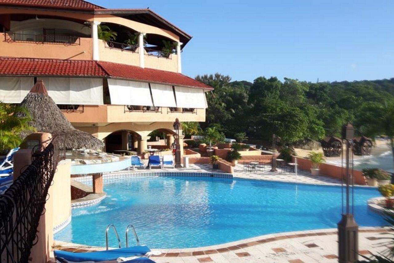 Un hôtel doté d’une piscine, de chaises longues et d’une structure dont le toit est fait de chaume.