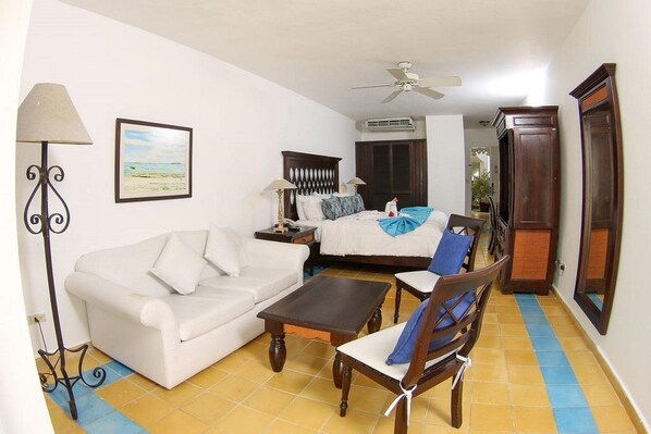 A room with a bed, a white sofa, a wooden chair, a table, a lamp, and a ceiling fan. - Sosua Bay Resort (Sosua)