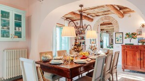 A dining area with a wooden table set for four, surrounded by chairs. A rustic ceiling and exposed beams are visible above.