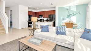 A modern living room with a sofa, coffee table, and a kitchen in the background. - Waterfront Family Mansion w BBQ, Games Room & Pool (Kissimmee)