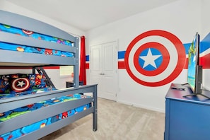 Una cama litera infantil con ropa de cama de superhéroes, un mural de Capitán América y un televisor sobre un mueble azul.