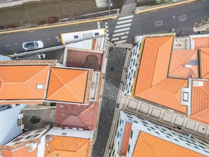 An aerial view of a street with buildings having orange tiled roofs, a pedestrian crossing, and a parked car.
