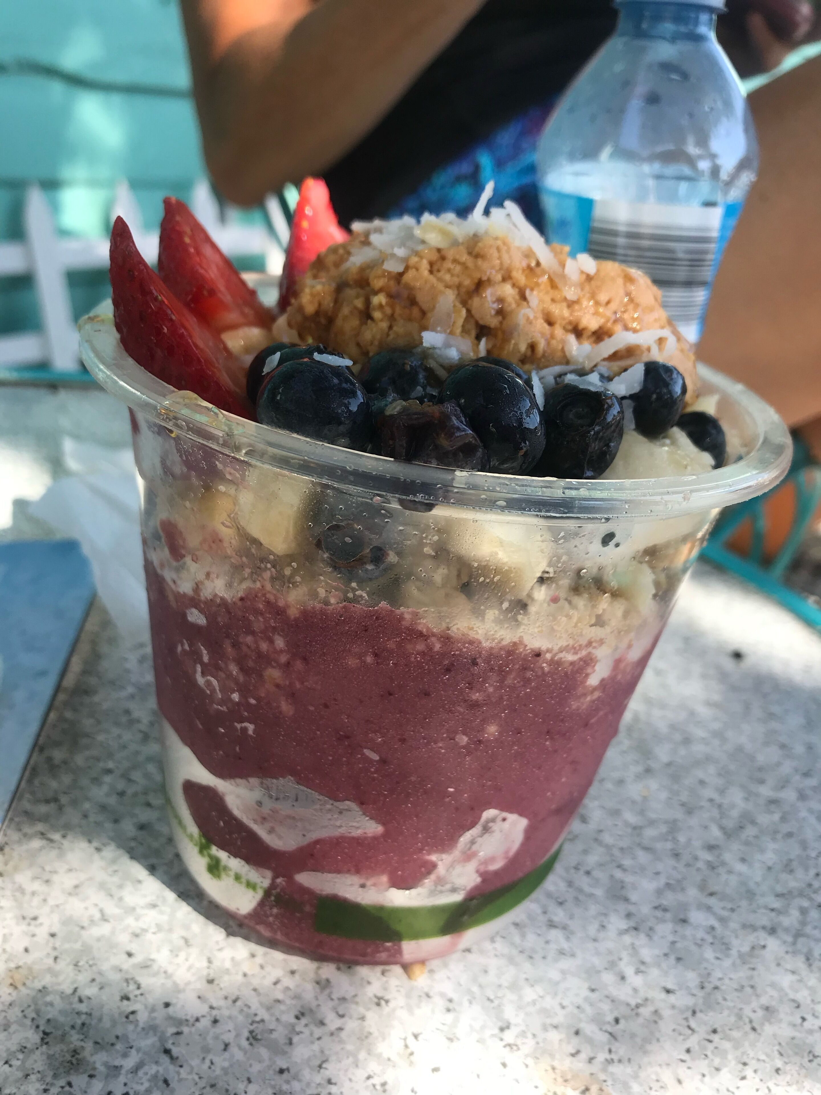 Postre en capas en vaso de plástico transparente con fresas, arándanos y coco rallado.