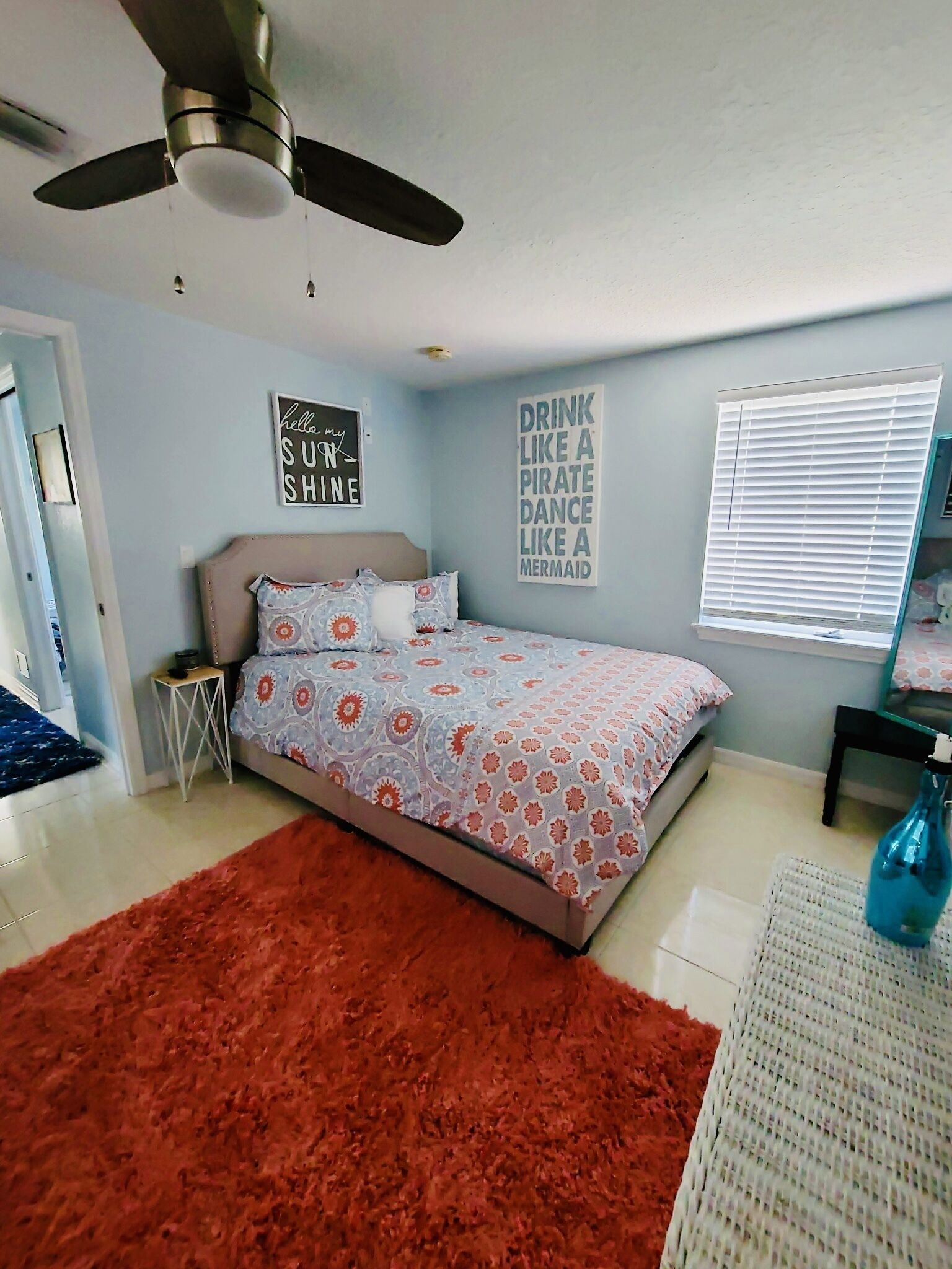 Une chambre à coucher comprenant un lit, un ventilateur de plafond, un tapis et deux éléments de décoration murale.